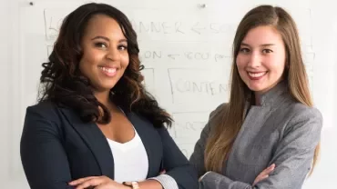 Deux femmes souriantes devant un tableau blanc.