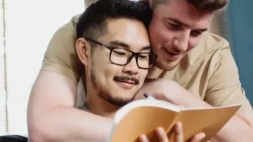 Two people smiling while reading a book together.