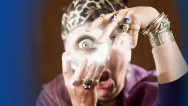 Person with rings and headscarf looking through magnifying glass, surprised expression.