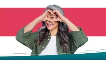 Smiling woman making a heart shape with her hands against a red background.