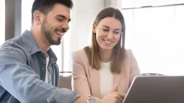 Deux personnes sont assises à une table devant un ordinateur portable en souriant.
