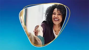 Woman smiling while shaking hands with another person against a blue background.