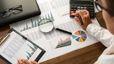 Personne analysant des graphiques de données avec calculatrice et loupe.