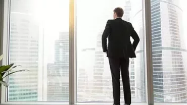 Businessman looking out at cityscape through office window.