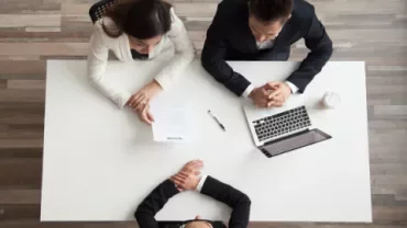 Sollicitatiegesprek met drie mensen aan tafel, documenten en een laptop zichtbaar.