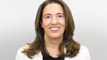 Femme souriante avec de longs cheveux bruns dans un blazer blanc.