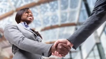 Two businesspeople shaking hands in a modern office building.