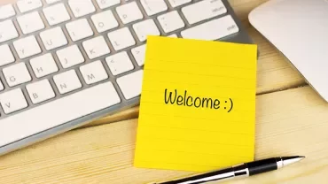 Gele notitie met 'Welcome :)' naast een toetsenbord en pen.