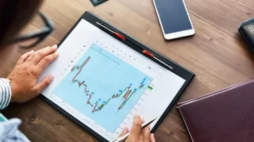 Person analyzing financial graphs on a tablet next to a smartphone and notebook.