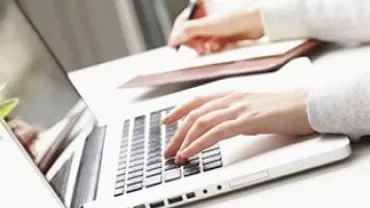Une personne tape sur un ordinateur portable et prend des notes, vue rapprochée.