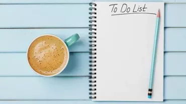 To-do list on a notepad with pencil and coffee on a blue table.