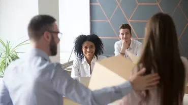 Een groep collega's in een vergaderruimte die praten en glimlachen.