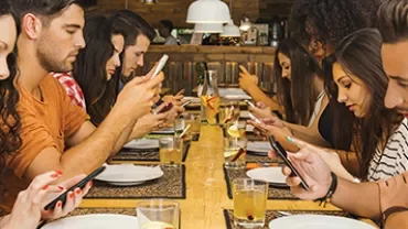 Des personnes assises à une table, concentrées sur leurs smartphones.
