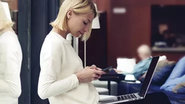 Femme utilisant un smartphone et un ordinateur portable dans un cadre moderne.