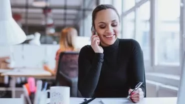 Femme au bureau parlant au téléphone et prenant des notes.