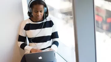 Person wearing headphones, using a laptop by a window.