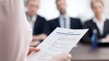 Persoon houdt een cv vast, tegenover een panel van interviewers.