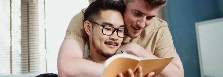 Two people smiling while reading a book together.