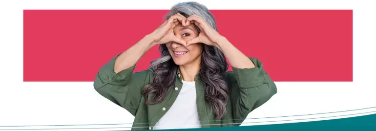 Smiling woman making a heart shape with her hands against a red background.