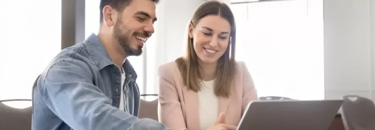 Deux personnes sont assises à une table devant un ordinateur portable en souriant.