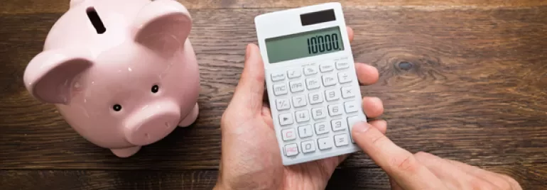 Personne utilisant une calculatrice près d'une tirelire et de piles de pièces.