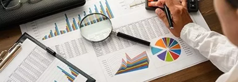 Persoon analyseert gegevensgrafieken met rekenmachine en vergrootglas.