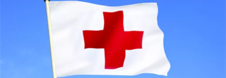 Red Cross flag waving against a clear blue sky.