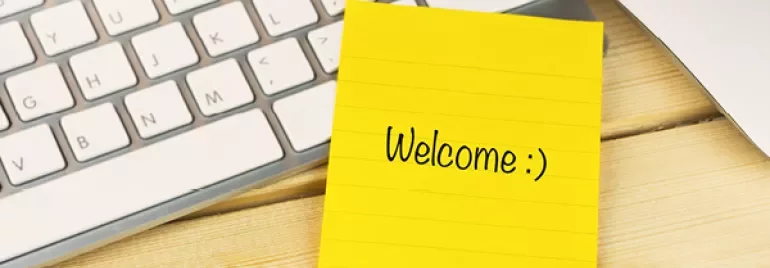 Gele notitie met 'Welcome :)' naast een toetsenbord en pen.