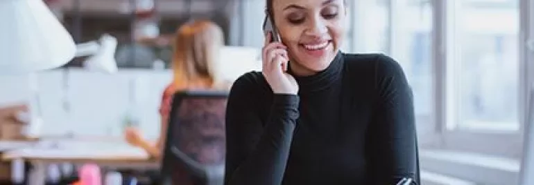 Femme au bureau parlant au téléphone et prenant des notes.