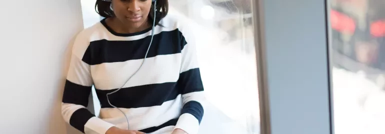 Person wearing headphones, using a laptop by a window.