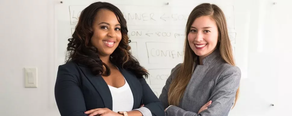 Two women standing in front of a whiteboard, smiling confidently.