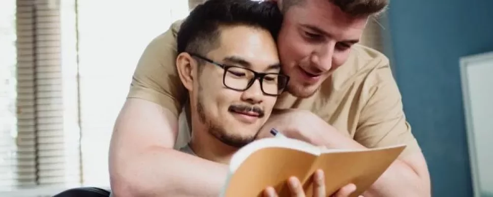 Two people smiling while reading a book together.