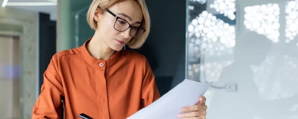 Femme blonde portant des lunettes lisant une feuille de papier