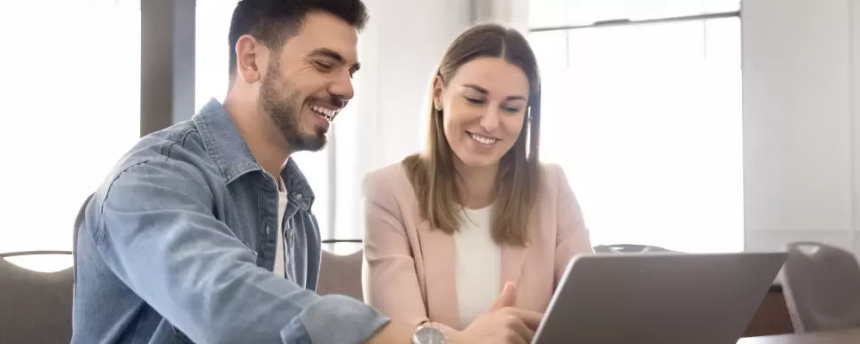 Deux personnes sont assises à une table devant un ordinateur portable en souriant.