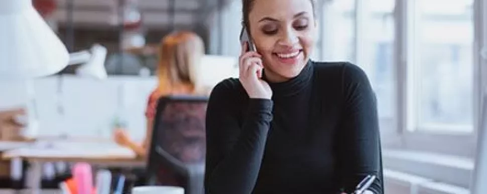 Woman in office talking on phone and writing notes.