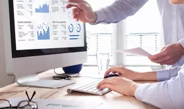 Two people analyzing financial reports on a computer screen.