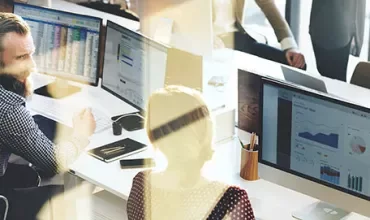 People working at desks with computers showing charts