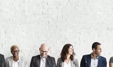 Group of diverse people sitting against a white brick wall.