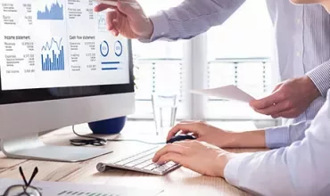 Two people analyze financial data on a computer screen.