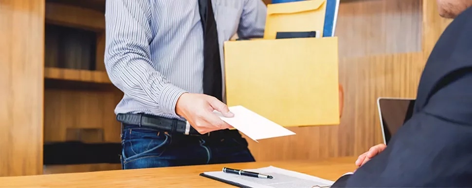 Person handing an envelope to a seated colleague in an office setting.