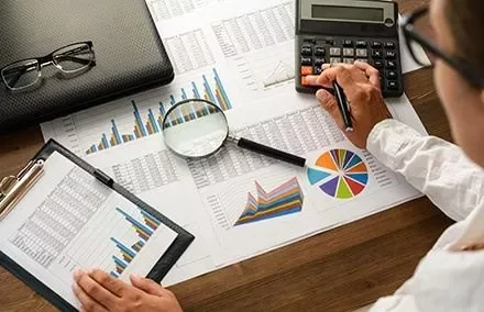 Persoon analyseert gegevensgrafieken met rekenmachine en vergrootglas.