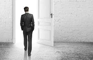 Man in a suit walking through an open door into a bright space.