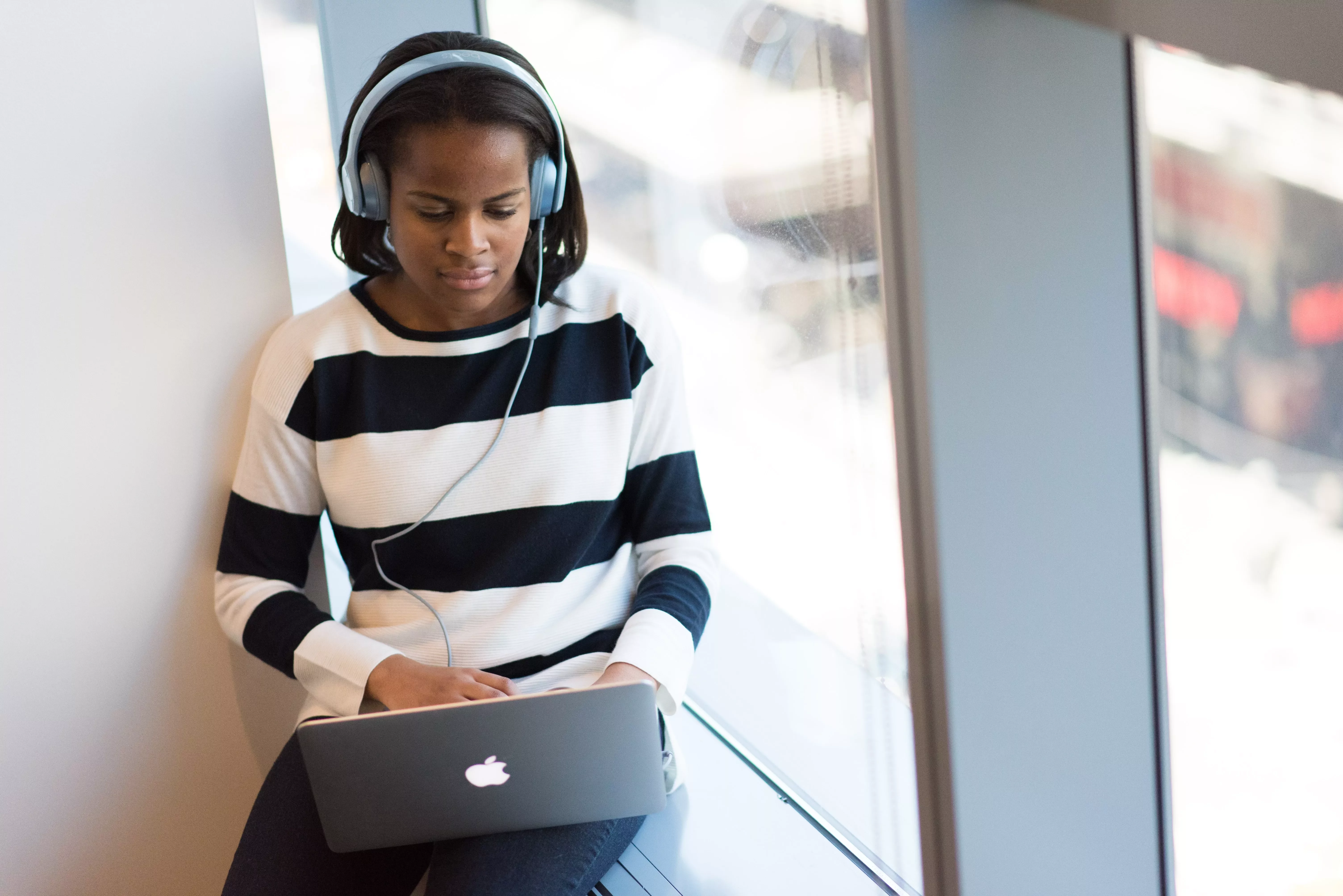 Person wearing headphones, using a laptop by a window.
